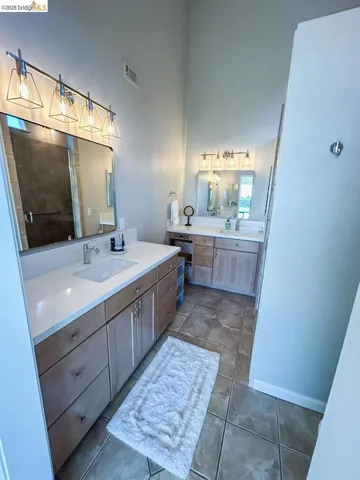 Dual vanity bathroom featuring light wood cabinetry with brushed nickel hardware, white countertops, and contemporary light fixtures