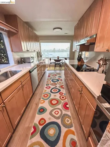 Galley kitchen featuring light wood cabinetry, white countertops, built-in cooktop, undermount sink, and wood-finish flooring