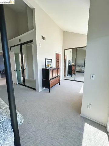 Spacious room featuring vaulted ceilings, light-colored carpeting, and ample natural light
