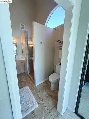 Bathroom featuring a private toilet alcove with an arched clerestory window, tiled flooring, wood-finish vanity with countertop, and a glass-enclosed shower
