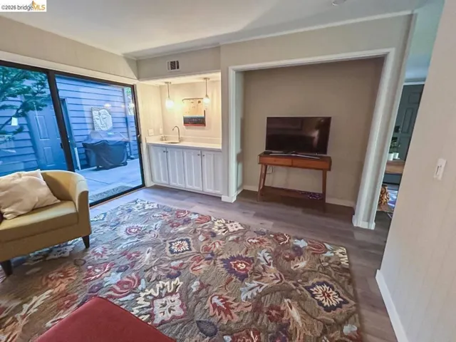 Living area featuring wood-finish flooring and a built-in wet bar with white cabinetry, a sink, and pendant lighting