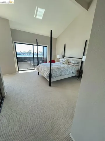 Spacious room featuring vaulted ceilings, a large sliding glass door, a private balcony, and light-toned carpet flooring
