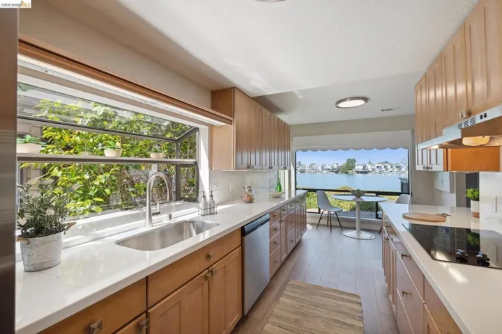 Galley kitchen featuring light wood-finish cabinetry, light countertops, wood-finish flooring, a built-in stainless steel sink with a gooseneck faucet, and a large window overlooking a waterway