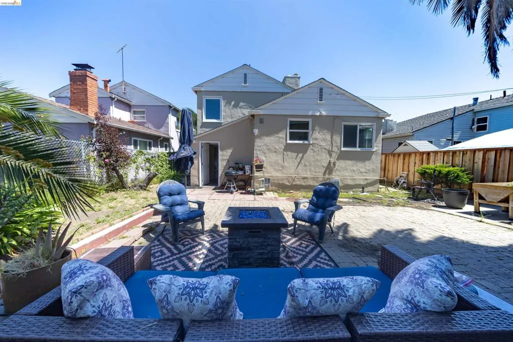 Expansive backyard featuring a paver patio with a built-in fire pit, stucco exterior, and a wood privacy fence