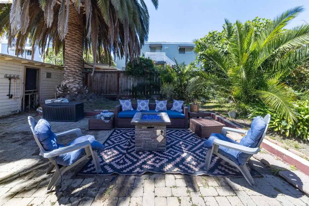 Expansive brick paver patio featuring mature palm trees, a detached storage building, and a wood privacy fence
