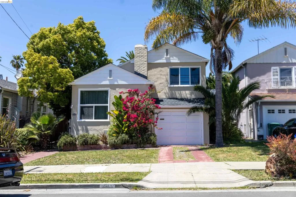 Stucco exterior residence featuring a white garage door, a prominent palm tree, and a brick-lined driveway