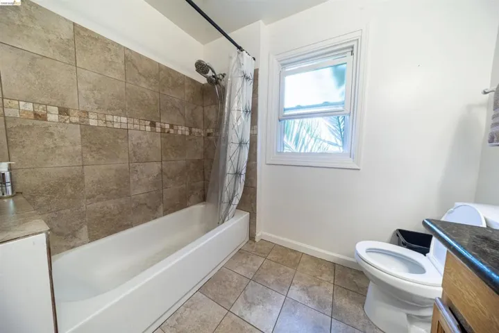 Bathroom featuring a tiled shower surround with decorative accent band, a white tub, a white framed window, and tiled flooring