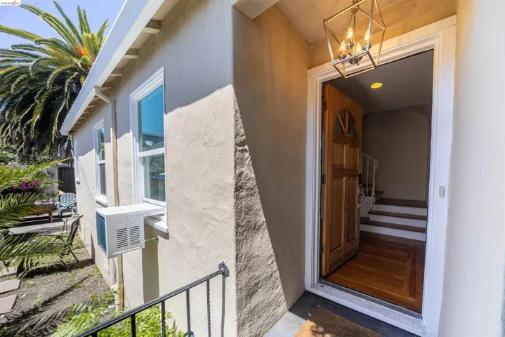 Exterior entry with a wood-paneled door, brass geometric chandelier, and stucco siding