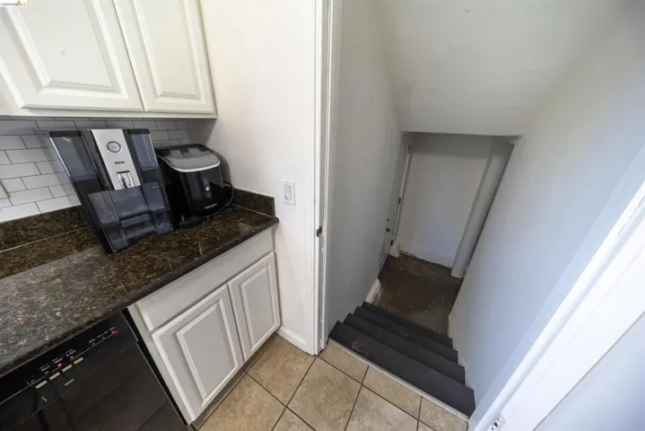 Kitchen area featuring light-toned cabinetry with dark hardware, a dark countertop, white subway tile backsplash, and a black dishwasher