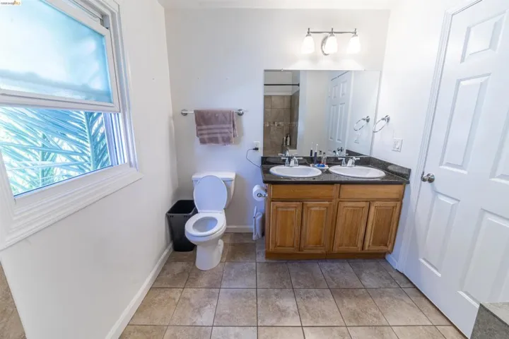 Bathroom featuring a double vanity with wood cabinetry and dark countertops, dual oval sinks, a large wall-mounted mirror, and a three-light fixture