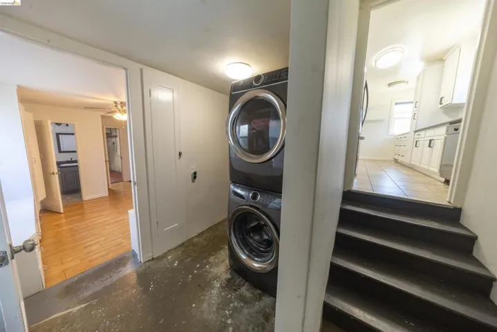 Dedicated laundry area featuring a stacked washer and dryer, adjacent to a room with wood-finish flooring and a partial bathroom vanity