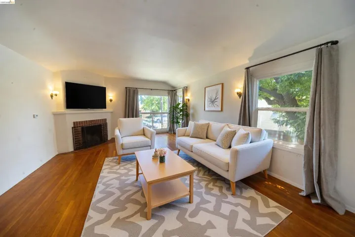 Living room featuring wood-finish flooring, a fireplace with brick surround, and wall-mounted sconces