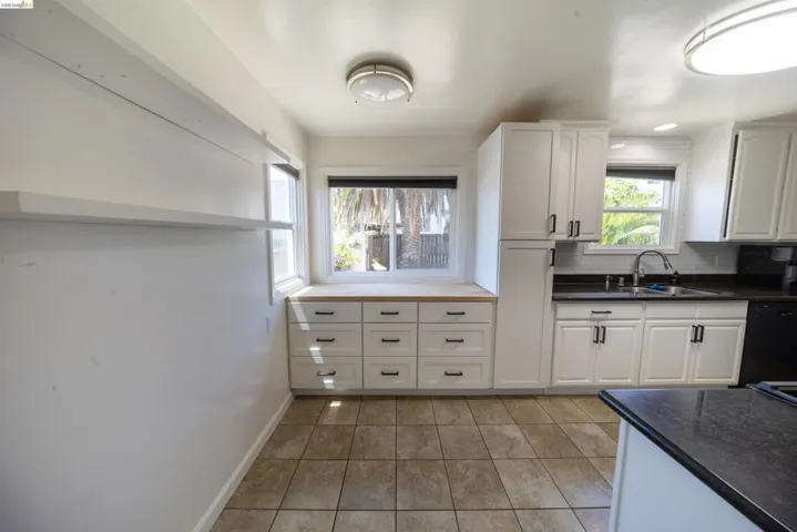 Kitchen featuring white cabinetry, dark countertops, a stainless steel sink with a gooseneck faucet, tile flooring, and a subway tile backsplash