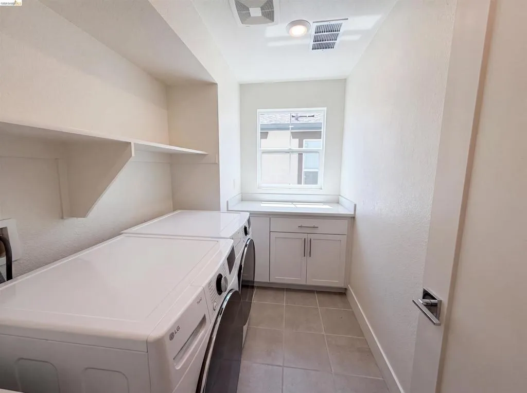 Dedicated utility space featuring tiled flooring, a window, white cabinetry with a countertop, and built-in shelving