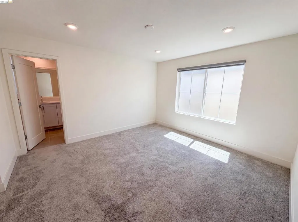 Carpeted room featuring a large window with roller shades, recessed lighting, and a white baseboard trim