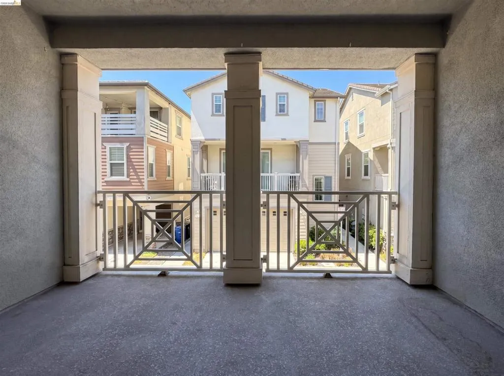Balcony with concrete flooring and decorative metal railings, framed by two support columns, overlooking multi-story residential properties