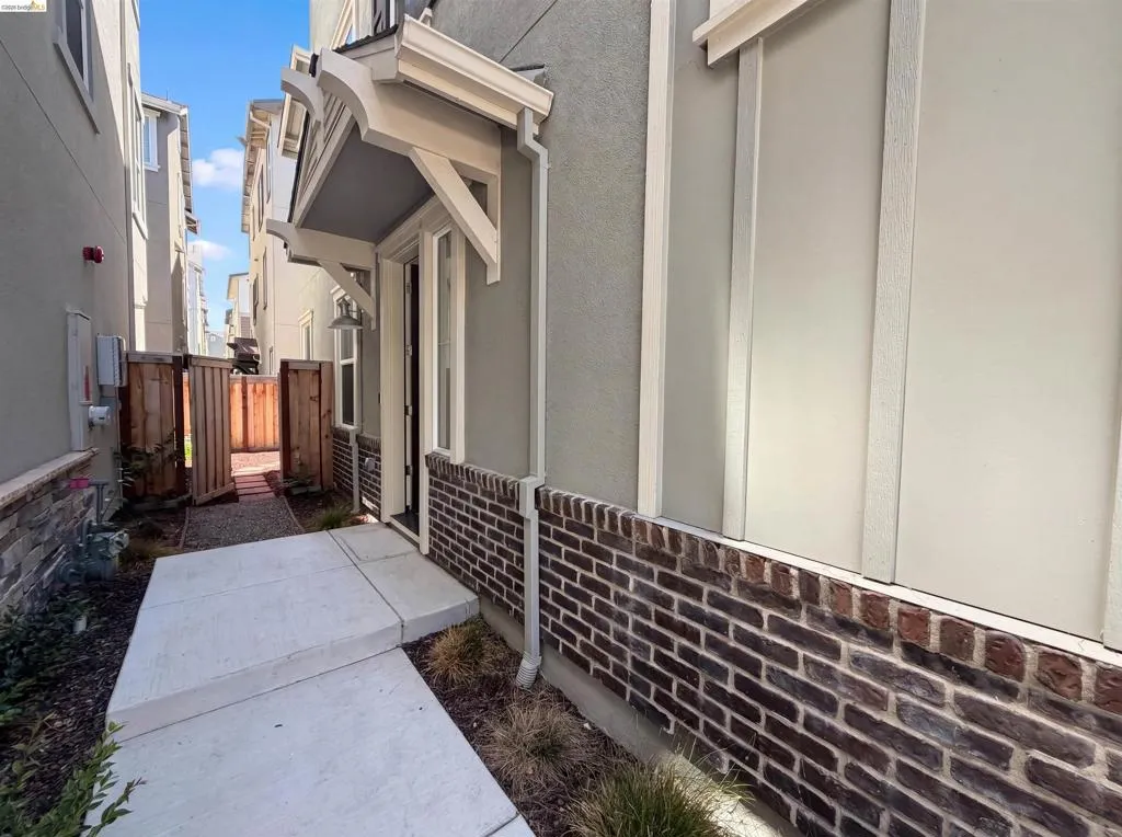 Entryway featuring a decorative overhang, board and batten siding, dark brick wainscoting, and a concrete pathway leading to a wooden gate