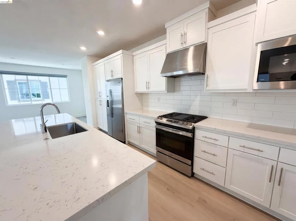 Modern kitchen featuring a large island with an undermount sink, stainless steel appliances, white shaker cabinetry, white subway tile backsplash, and light wood-finish flooring