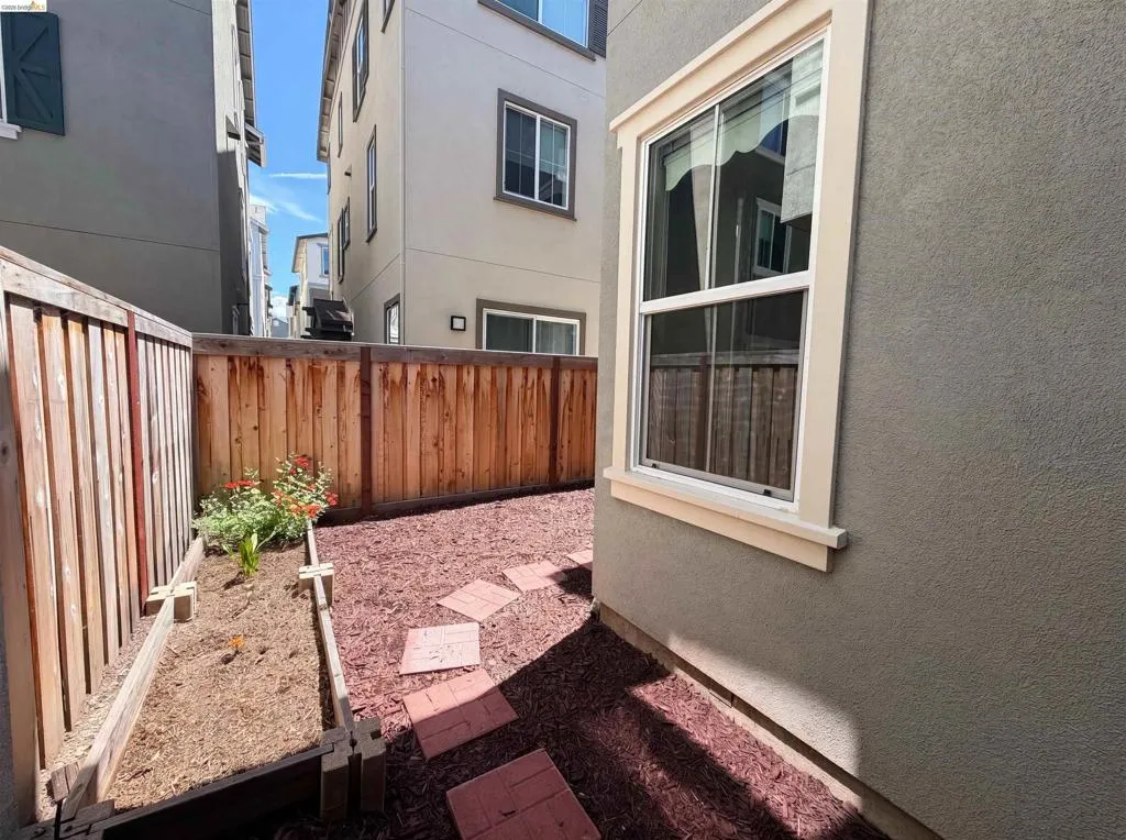 Private outdoor space featuring a wood fence, raised garden bed with plantings, red mulch ground cover, and stepping stones