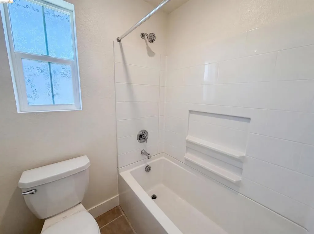 White subway tile tub surround featuring a recessed niche with integrated shelving, chrome fixtures, and a privacy window