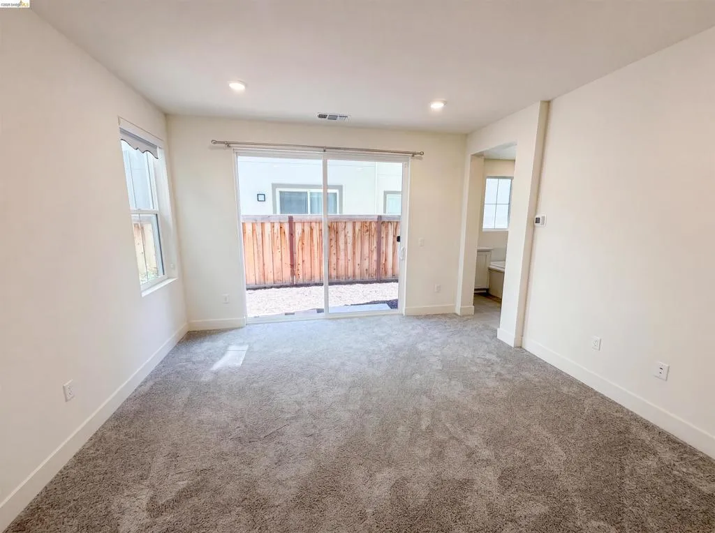 Spacious room featuring neutral carpeting, recessed lighting, and a large sliding glass door opening to a private outdoor area