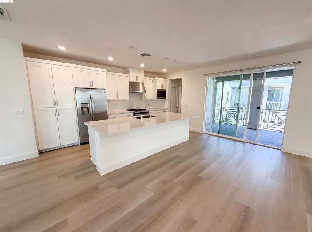 Contemporary kitchen featuring a large central island with a light-toned countertop, white cabinetry, stainless steel appliances, and wood-finish flooring