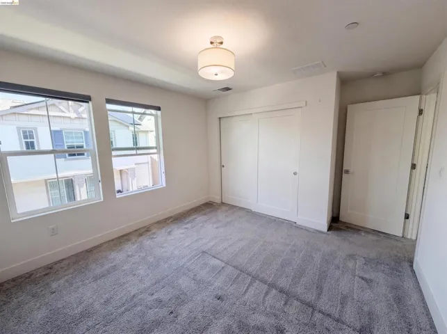 Bright room featuring two large windows with roller shades, light gray carpeting, and a flush-mount ceiling light fixture
