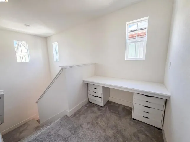 Integrated desk with built-in drawers, large window, additional windows, white wall finishes, and gray carpet