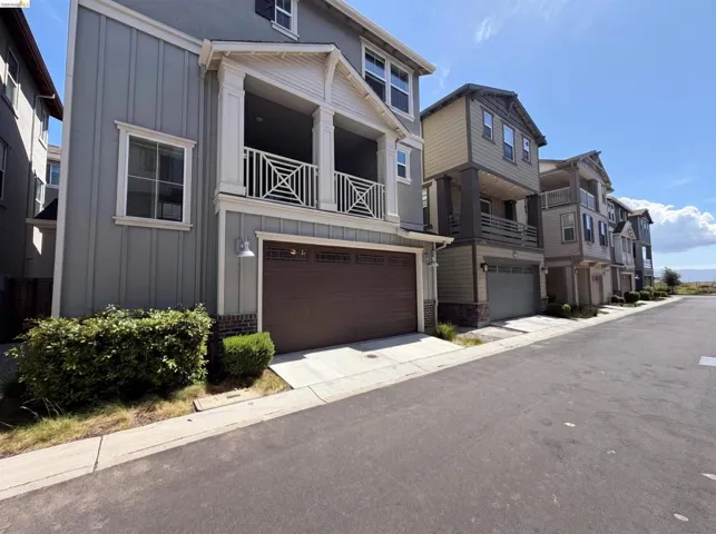 Contemporary multi-level residence featuring board and batten siding, a prominent balcony with decorative railing, and an integrated garage with a paneled door
