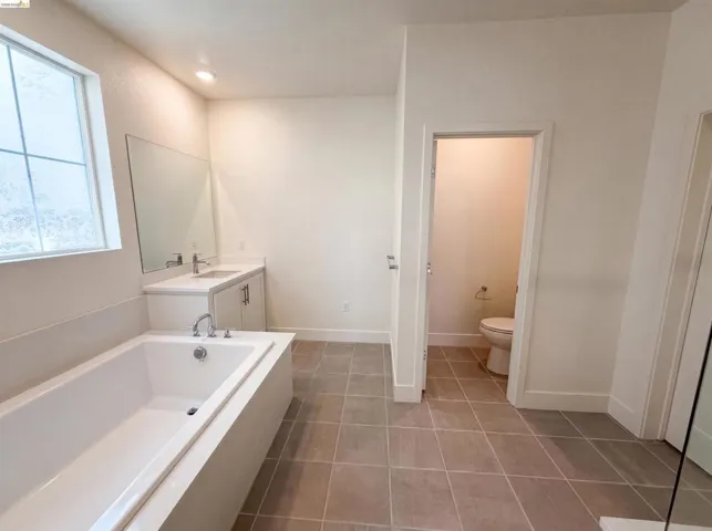 Modern bathroom featuring a built-in soaking tub, a single vanity with a white countertop, and contemporary tile flooring