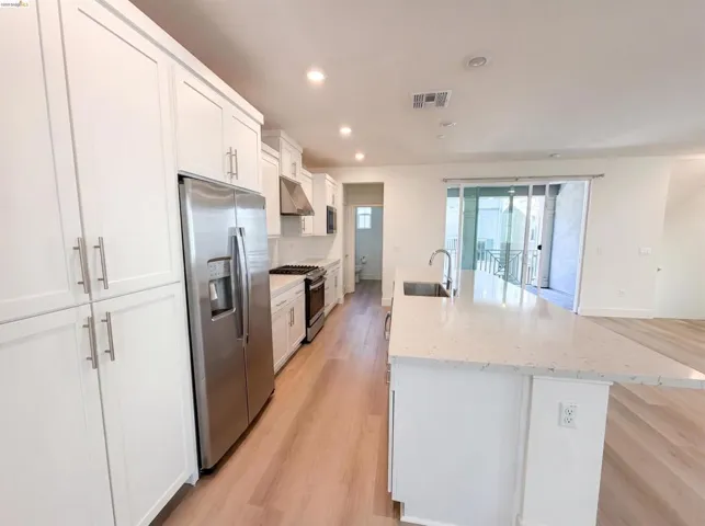 Modern kitchen featuring white shaker cabinetry, stainless steel appliances, a white tile backsplash, and light wood-finish flooring