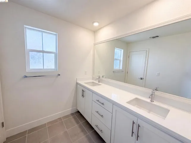 Double vanity with white cabinetry, integrated sinks, chrome fixtures, and a large wall-mounted mirror
