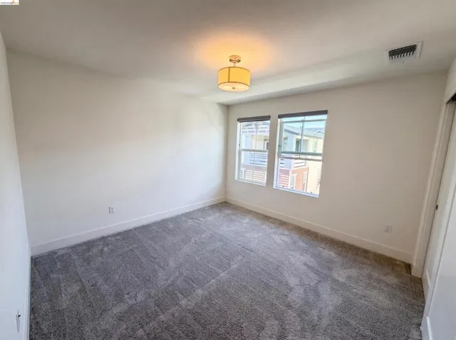 Bright room featuring two large windows, gray patterned carpeting, white baseboards, and a drum-style ceiling light fixture