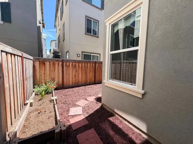 Private outdoor space featuring a wood fence, raised garden bed with plantings, red mulch ground cover, and stepping stones