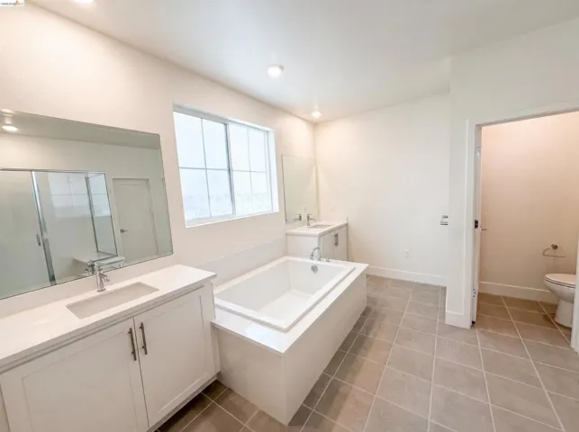 Spacious bathroom with dual vanities, white cabinetry, integrated sinks, a built-in bathtub, and tiled flooring
