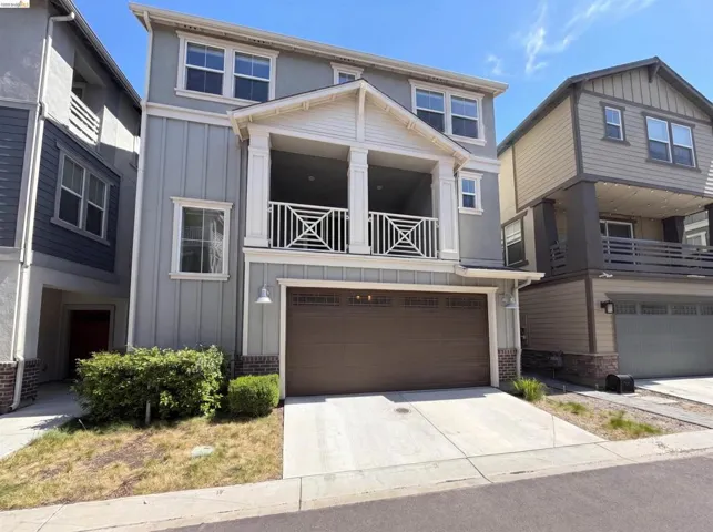 Three-story residence featuring a covered balcony with decorative railing, a two-car garage, and a covered entry with columns