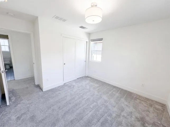 Spacious room featuring light gray patterned carpet, white walls, a single window, a semi-flush mount ceiling light, and white bi-fold closet doors