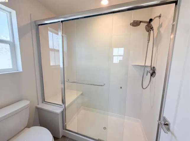 Walk-in shower featuring a sliding glass door, integrated bench, and dual showerheads