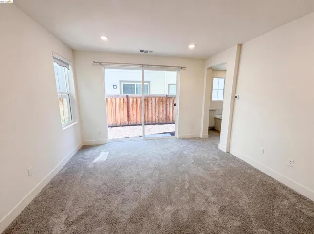Spacious room featuring neutral carpeting, recessed lighting, and a large sliding glass door opening to a private outdoor area