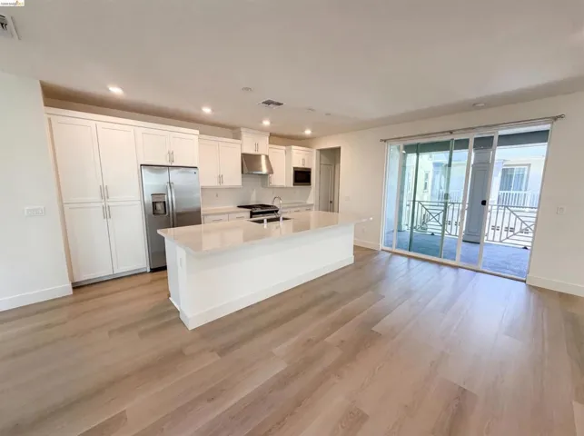 Contemporary kitchen featuring a large central island with a light-toned countertop, white cabinetry, stainless steel appliances, and wood-finish flooring