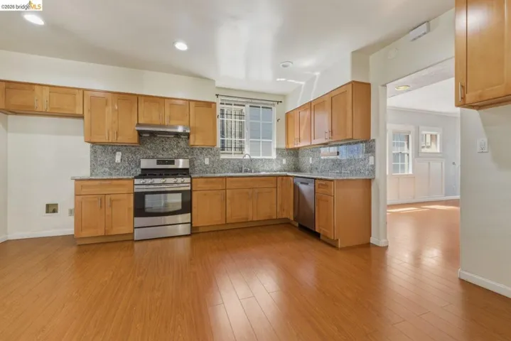 Kitchen featuring wood-finish flooring, wood cabinetry, stone-finish countertops, stainless steel appliances, and recessed lighting