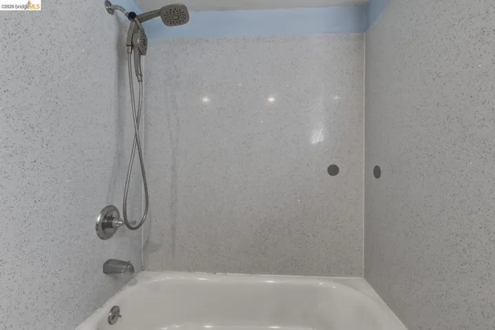 Bathtub and shower combination featuring white speckled shower surround panels, a built-in white tub, and brushed chrome fixtures