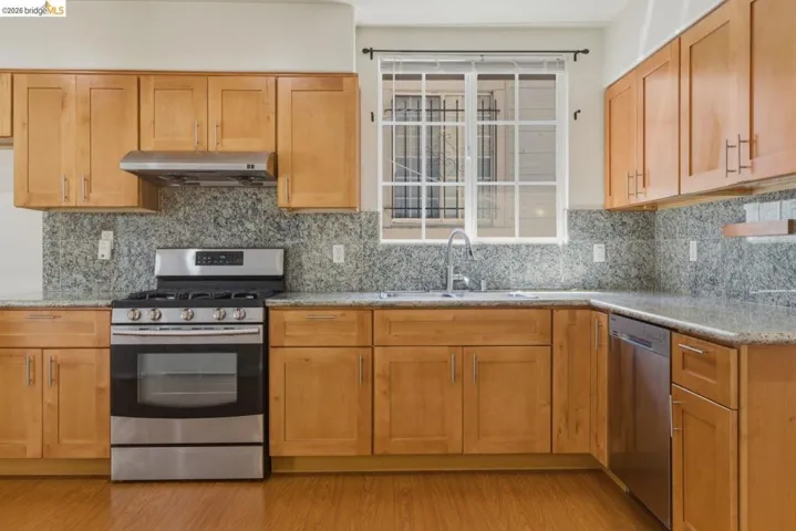 Kitchen featuring wood-finish cabinetry, granite countertops, stainless steel appliances, and a window with security bars