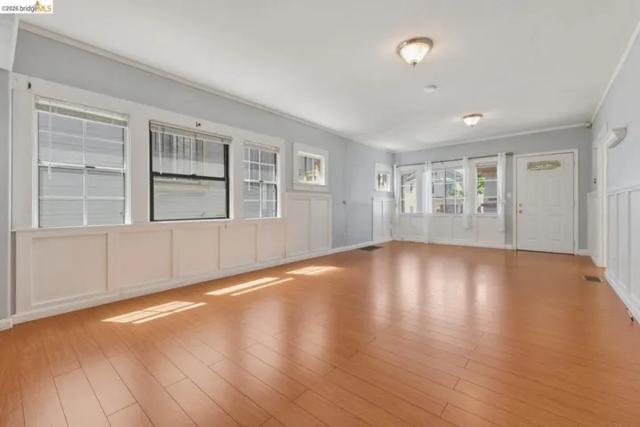 Expansive room featuring wood-finish flooring, white paneled wainscoting, and multiple windows