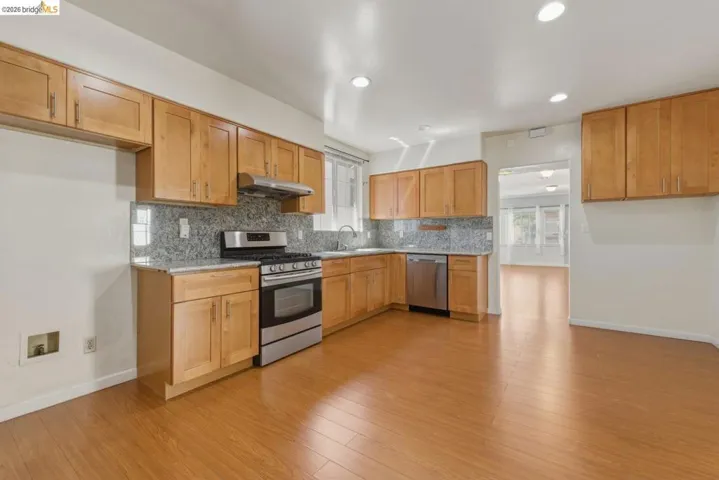 Kitchen featuring wood-finish flooring, light wood cabinetry, stone countertops with a matching backsplash, stainless steel appliances, and recessed lighting