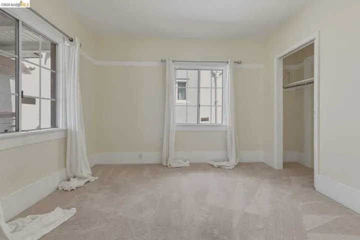Carpeted room featuring multiple windows with grid patterns, a closet with a hanging rod, and light-toned walls with contrasting trim