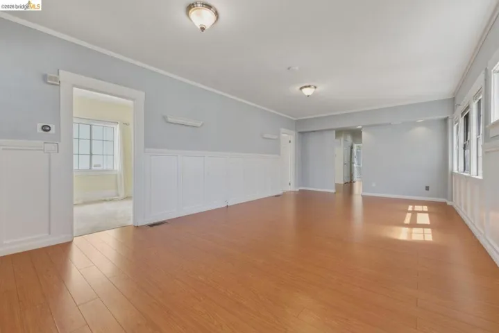 Spacious room featuring wood-finish flooring, white wainscoting, light blue walls, and multiple windows