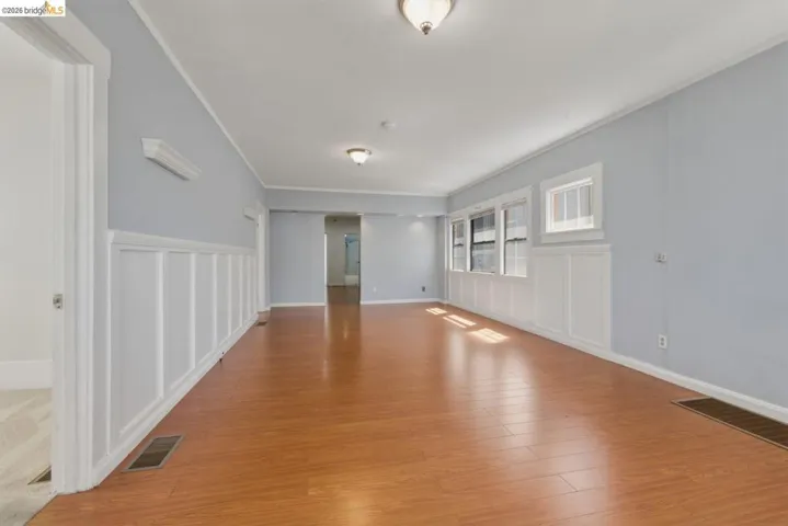 Spacious room featuring wood-finish flooring, white wainscoting, light blue walls, and multiple windows