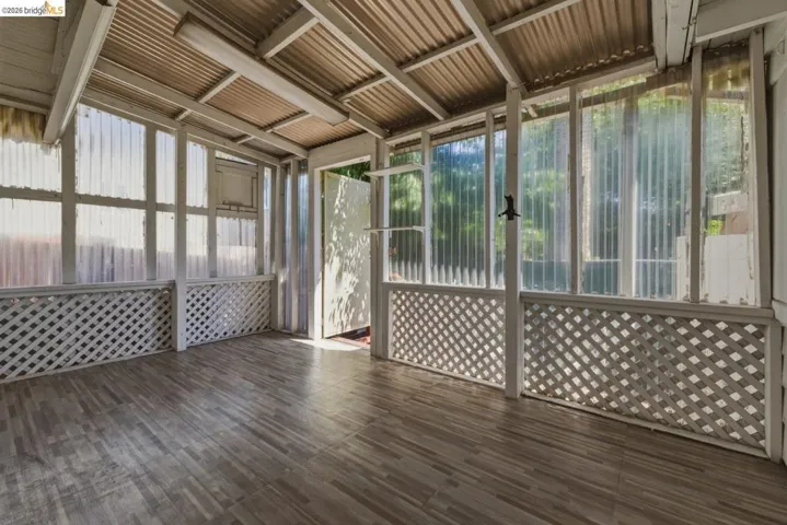 Enclosed porch featuring corrugated translucent panels, white lattice detailing, and wood-finish flooring