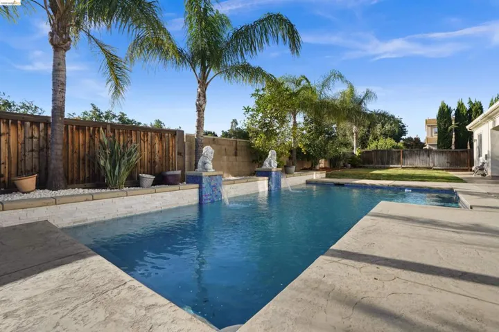 Outdoor swimming pool featuring a waterfall accent, patterned concrete decking, and a manicured lawn area
